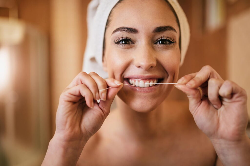 Smiling woman flossing her teeth in the bathroom - oral health in curacao