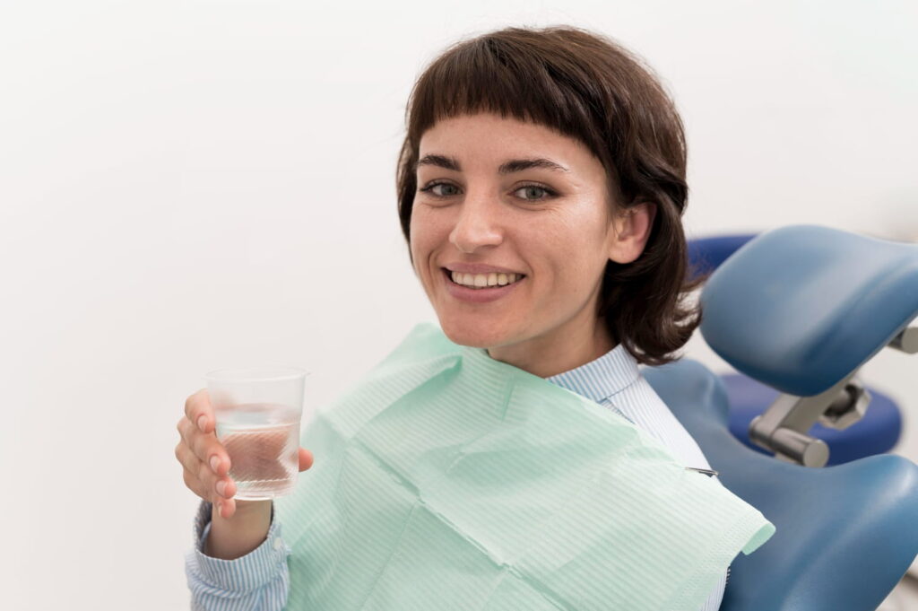 Smiling dental patient holding a glass of water, illustrating how tap water affects your teeth.